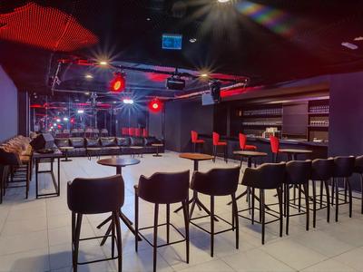 Elegante bar dell'hotel con illuminazione intensa, accenti rossi e sgabelli moderni.
