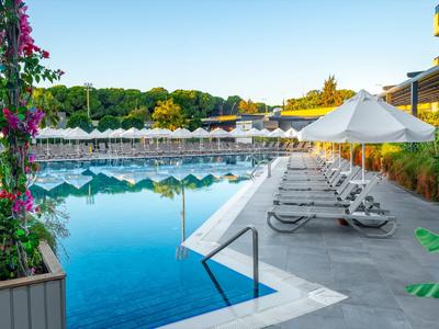 Spokojny hotelowy taras wypoczynkowy obok czystego niebieskiego basenu z parasolami i kwiatami.