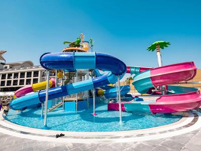 Toboganes de agua coloridos desembocan en una piscina junto a un resort bajo un cielo azul.