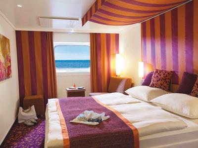 Habitación de hotel acogedora con cama doble, cortinas coloridas y vista al mar desde la ventana.