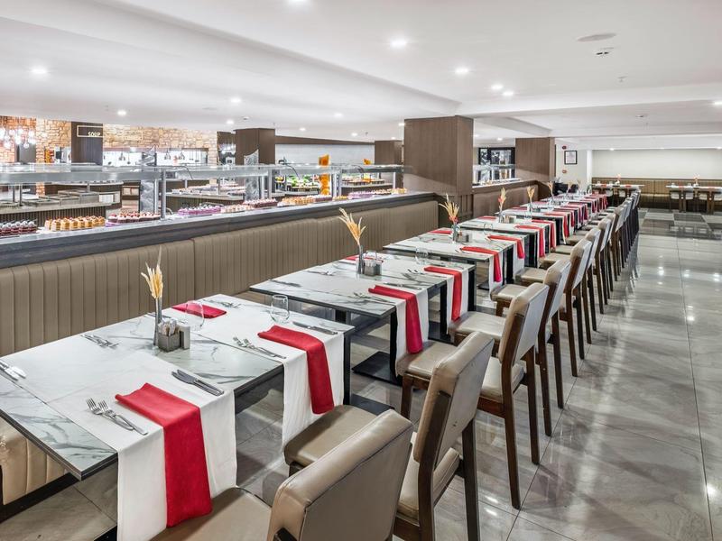 Mesa larga en restaurante con mesas blancas y caminos de mesa rojos.