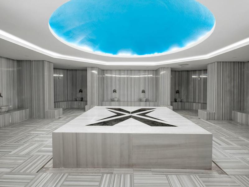 Sala de spa moderna con piscina central de mármol y luz azul en el techo.