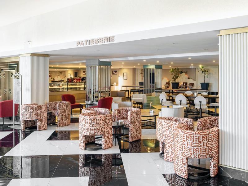 Área de comedor de hotel luminosa con sillas estampadas y suelo a cuadros en blanco y negro.