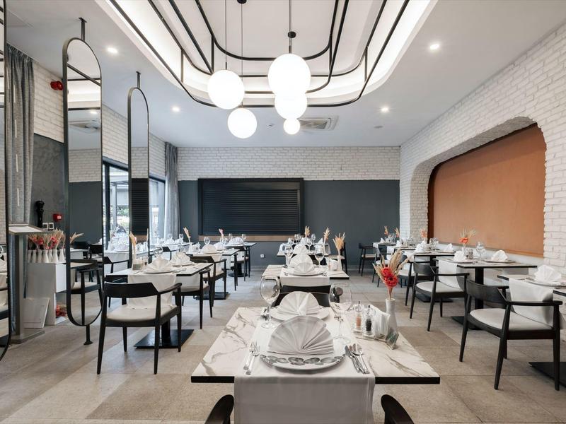 Restaurante moderno con paredes blancas, sillas negras y mesas elegantemente preparadas.