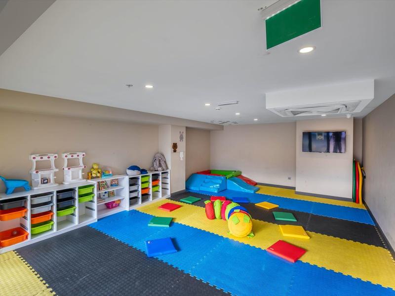 Un área de juegos infantil colorida con alfombras, cojines y estanterías llenas de juguetes en una habitación moderna.