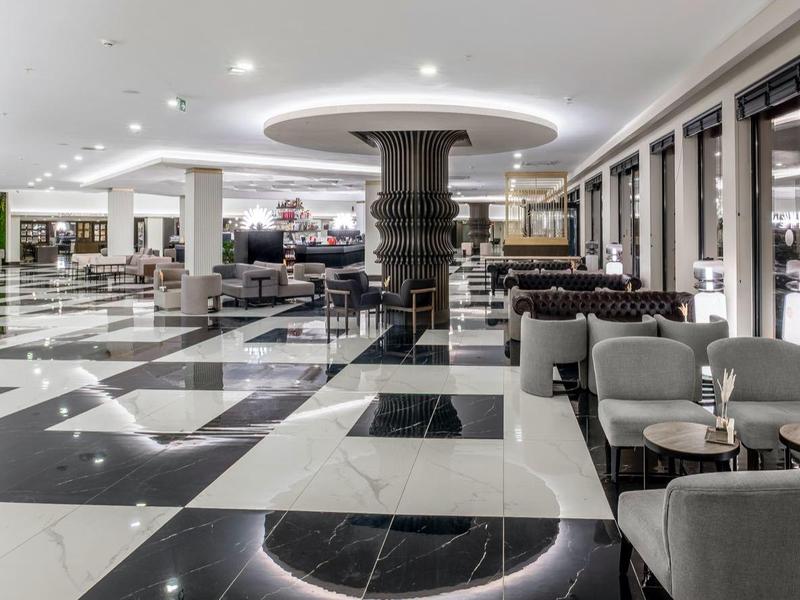 Amplio vestíbulo de hotel con suelo de mármol blanco y negro y zonas de asientos modernas.