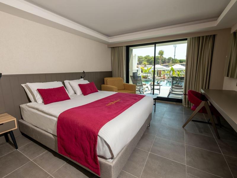 Habitación de hotel moderna con cama grande, ropa de cama rosa, escritorio y terraza con vista a la piscina.