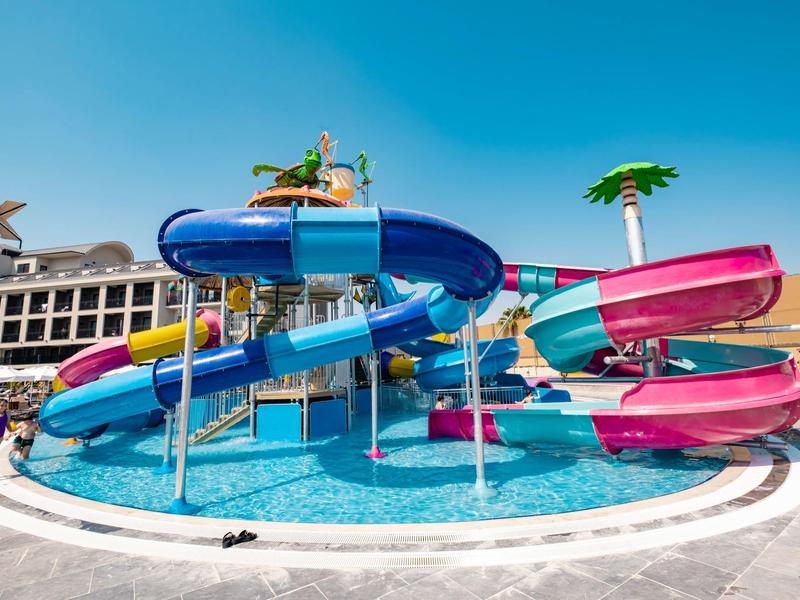 Toboganes de agua coloridos desembocan en una piscina junto a un resort bajo un cielo azul.