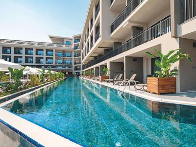 Piscine d'hôtel moderne avec chaises longues et parasols à côté d'un bâtiment à plusieurs étages.