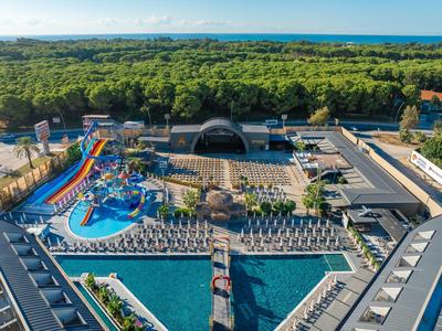 Grand parc aquatique avec plusieurs toboggans, piscine et transats près de la forêt et de la mer.