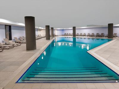 Une piscine intérieure moderne dans un hôtel avec des chaises longues et des piliers.