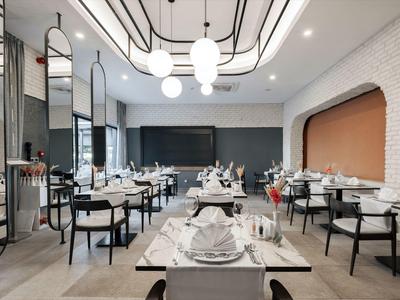 Restaurant moderne avec murs blancs, chaises noires et tables élégamment dressées.