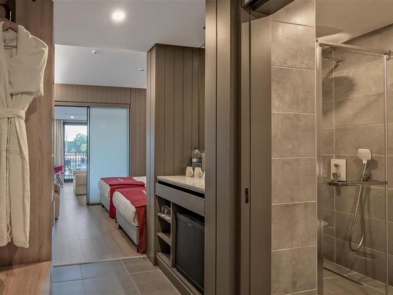 Chambre d'hôtel moderne avec détails en bois, grand lit et douche vitrée dans la salle de bain.