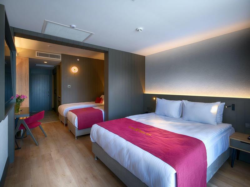 Chambre d'hôtel moderne avec deux lits, sol en bois et éclairage tamisé.