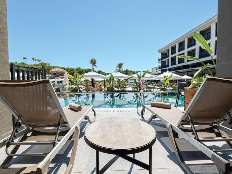 Vue depuis la terrasse avec chaises longues sur la piscine et l'hôtel sous un ciel dégagé.