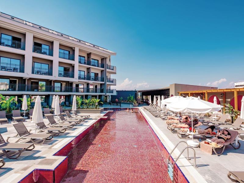 Piscine d'hôtel moderne avec carrelage rouge, transats et parasols sous un ciel clair.