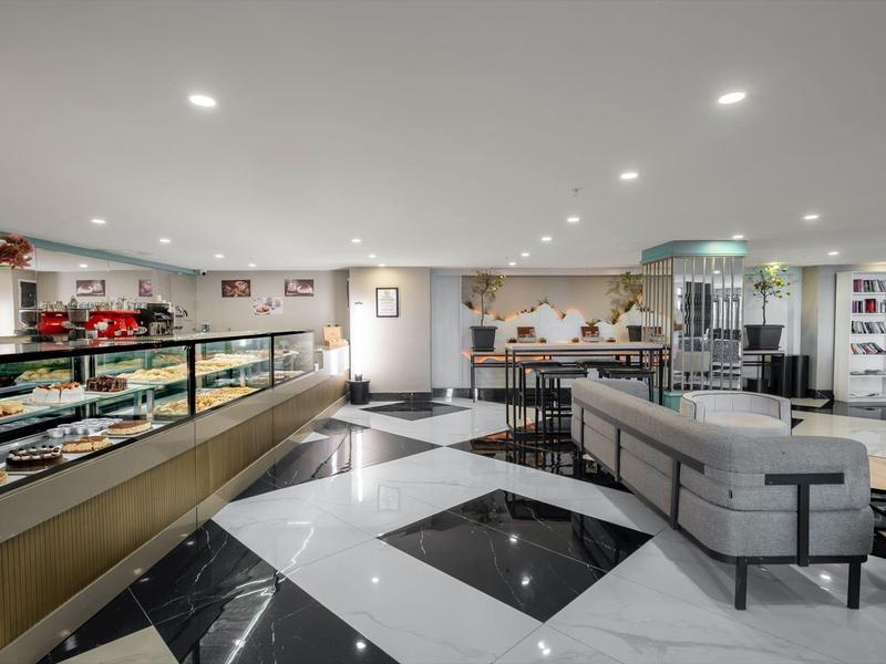 Hall d'hôtel moderne avec canapé gris, sol en marbre noir et blanc, et comptoir de petit-déjeuner