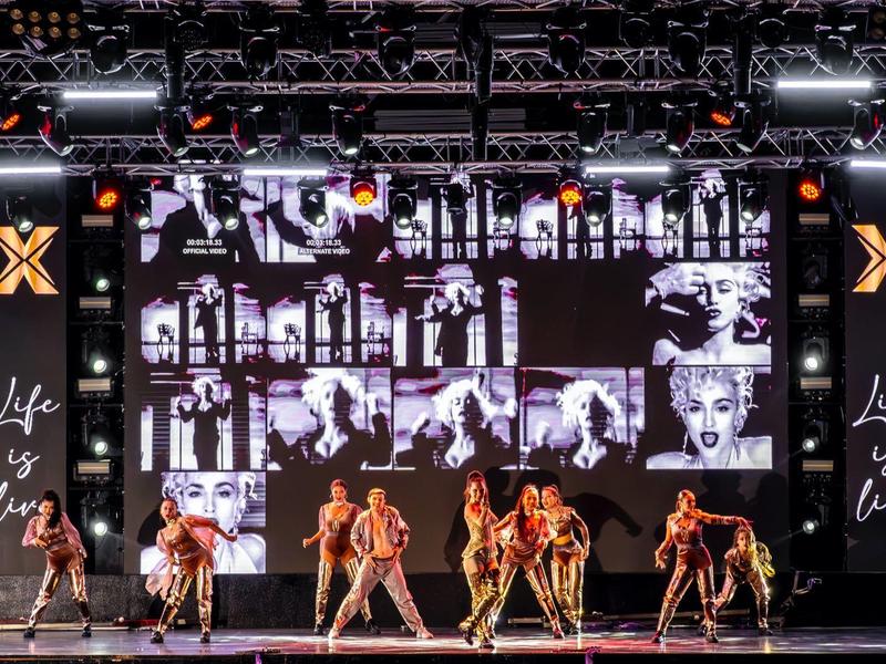 Une scène avec des danseurs en costumes dorés et de grands écrans en arrière-plan.