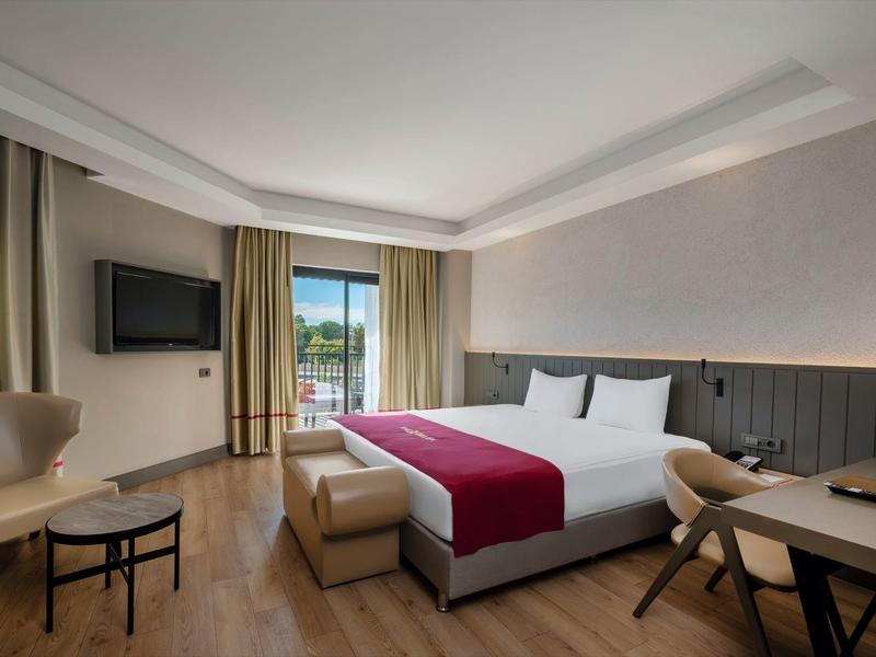 Chambre d'hôtel moderne avec grand lit, télévision, chaises et balcon avec vue extérieure.