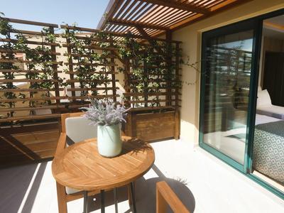 Balkon mit Holztisch, zwei Stühlen und einem Glas mit Blumen neben einem Schlafzimmer.