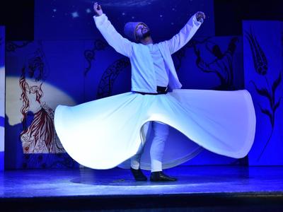Un danzatore derviscio che gira sul palco con abito bianco fluente.