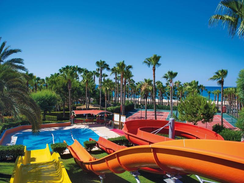 Wasserpark mit Rutschen, Pool und Liegestühlen vor blauem Himmel und Palmen