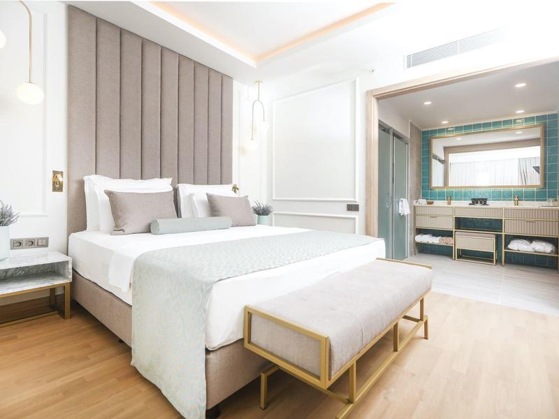 Helles modernes Hotelzimmer mit großem Bett, hellen Holzböden und angrenzendem Badezimmer.