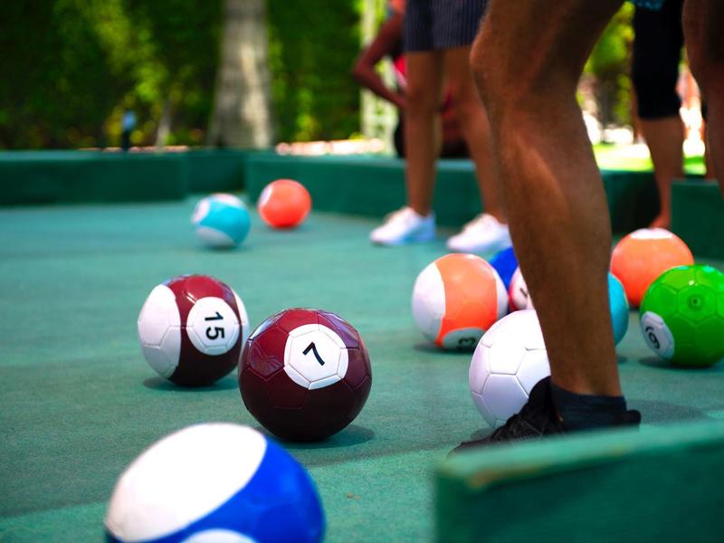 Mehrere Billardkugeln auf einem Outdoor-Billardtisch mit Personen im Hintergrund.