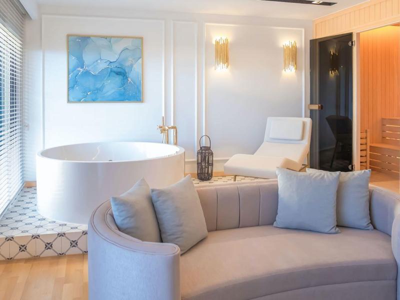 Modernes Hotelzimmer mit Sofa, freistehender Badewanne und Sauna im Hintergrund.