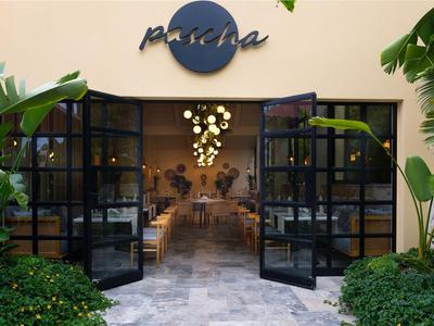 Puertas negras de vidrio abiertas conducen a un restaurante acogedor con plantas e iluminación decorativa.