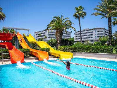 Toboganes acuáticos coloridos se extienden en una piscina con una persona nadando y palmeras al fondo.