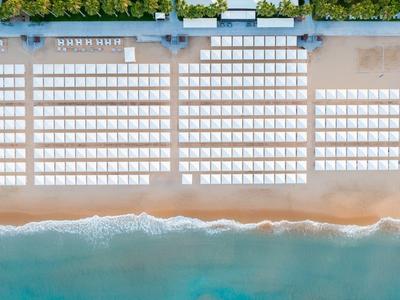 Vista aerea di una spiaggia con lettini e ombrelloni ordinati vicino al mare.