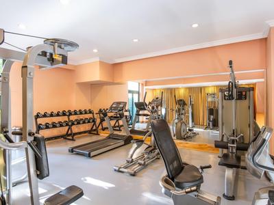 Palestra luminosa con varie attrezzature e manubri davanti a uno specchio grande.