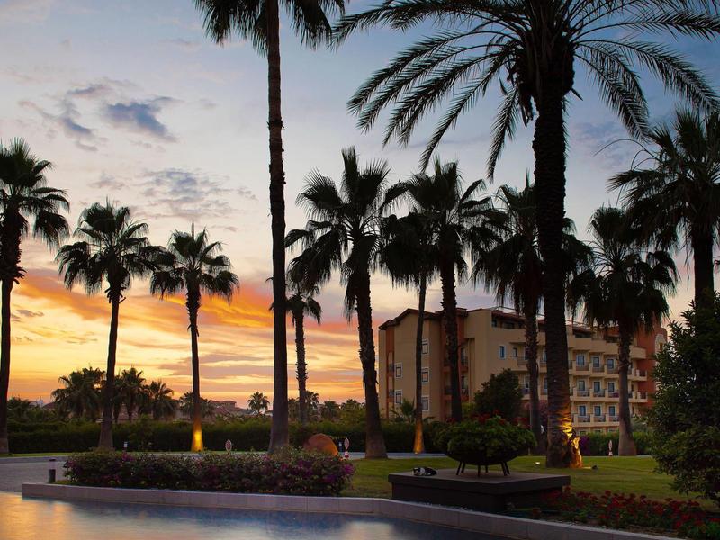 Palme davanti a un edificio dell'hotel al tramonto con cielo colorato