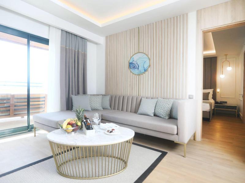 Soggiorno moderno con divano ad angolo grigio, tavolo rotondo e accesso al balcone in ambiente luminoso.