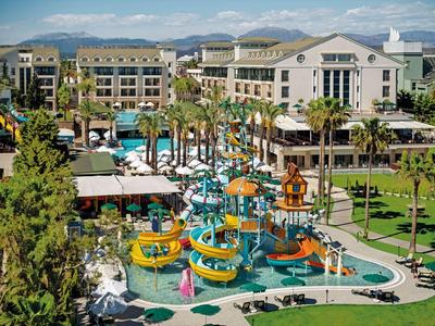 Resort hotel with colorful water slides and pools surrounded by palm trees and green lawns.