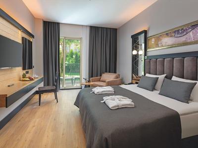 Modern hotel room with bed, armchair, balcony, and TV.