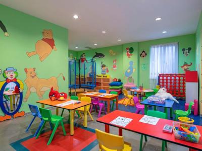 Bright, colorful children's playroom with tables, chairs, toys, and playful wall decorations.
