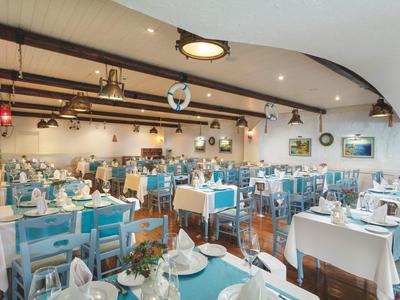 Spacious restaurant with blue chairs, white tablecloths, and elegant table settings under a vaulted ceiling.