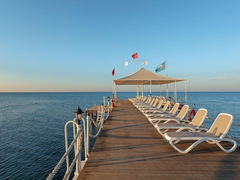 Wooden pier with sunbeds extending over calm sea under clear sky