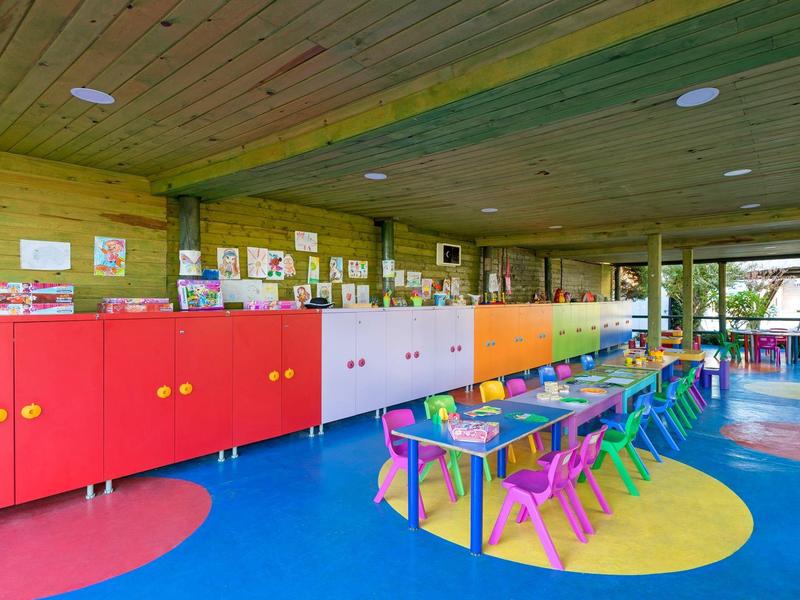 Colorful children's playroom with small tables, chairs, and storage cabinets in a wooden room.