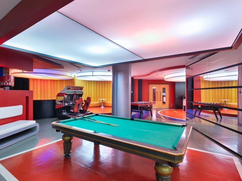 Modern game room with pool table, arcade games, and colorful lighting.