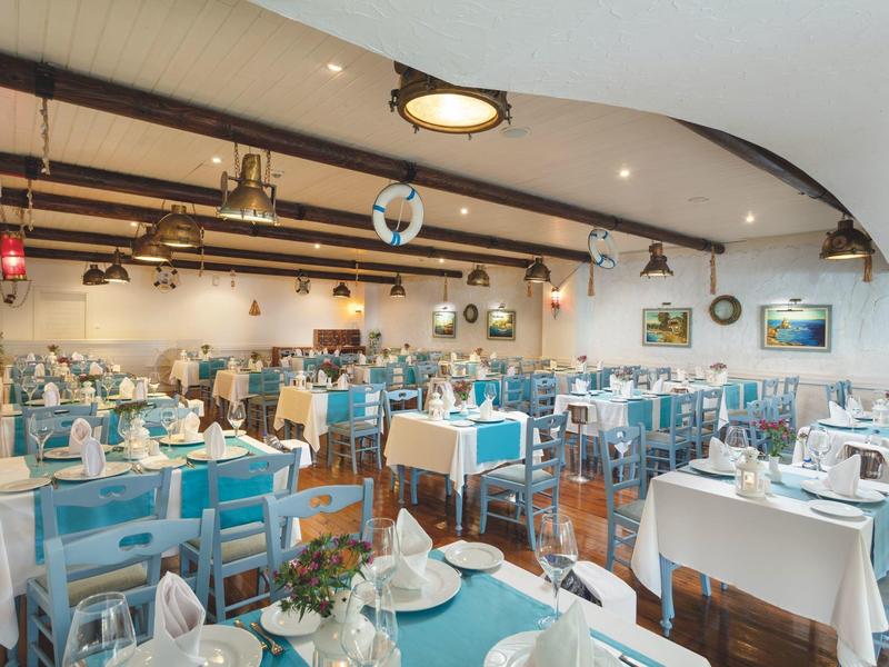 Spacious restaurant with blue chairs, white tablecloths, and elegant table settings under a vaulted ceiling.