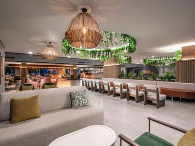 Espace lounge moderne avec canapés, plantes et éclairage suspendu.