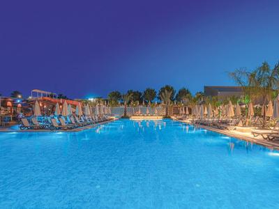 Piscine d'hôtel éclairée avec chaises longues et palmiers la nuit.