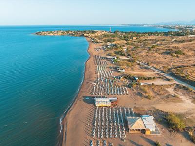 Luchtfoto van een lang zandstrand met rijen parasols en stoelen naast kalme blauwe zee.
