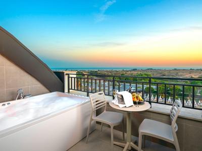 Buitenterras met witte jacuzzi, tafel, stoelen en uitzicht op zonsondergang over groen landschap.