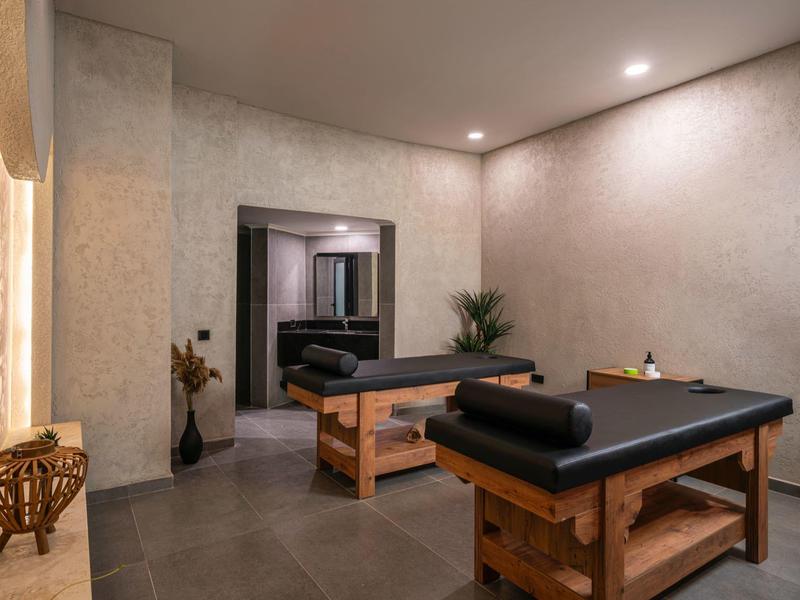 Gezellige massageruimte met houten tafel, opgerolde handdoeken, warme verlichting en minimalistische inrichting.