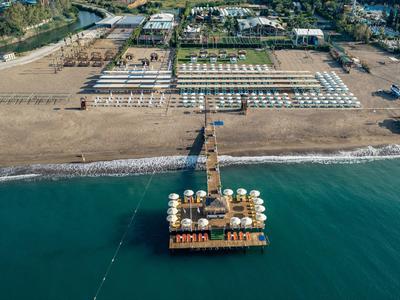 Luchtfoto van een lange houten pier met parasols en ligstoelen op het strand naast de zee.