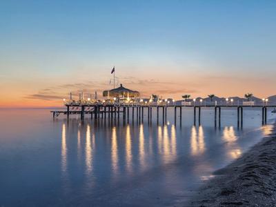Lange pier die zich uitstrekt in kalme zee bij zonsondergang met warme lucht en zachte golven op het strand.